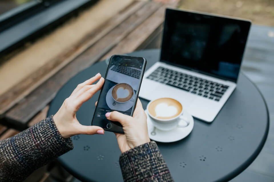 Person taking a photo of a coffee cup with a smartphone next to a laptop in a modern workspace. Your Website Is Your Most Powerful Marketing Asset